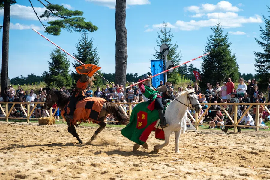 Two knights in colorful armor joust on horseback before a crowd at a medieval reenactment event.