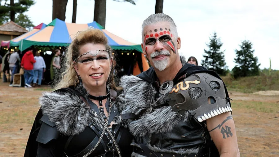 A man and woman dressed in Viking-inspired costumes with face paint and a colorful tent in the background at an outdoor event.