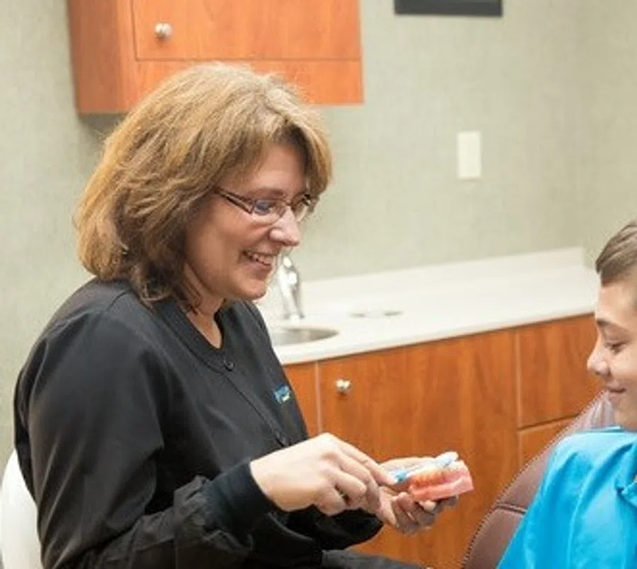 Dentist demonstrating proper brushing technique on a dental model to a young patient in a clinic.