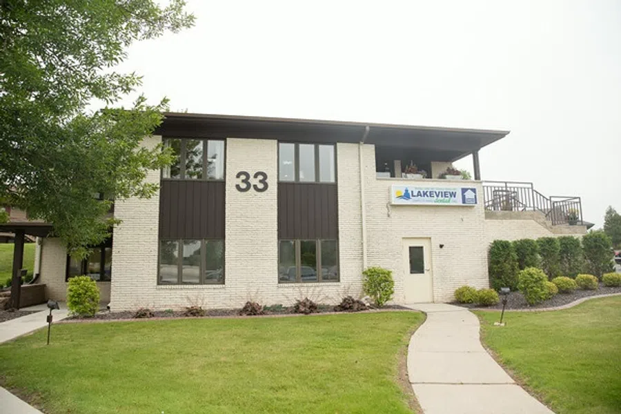 Two-story beige brick building with number 33 and Lakeview Apartments sign surrounded by green lawn and trees.