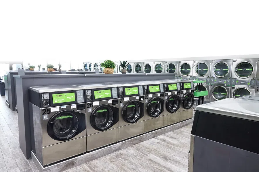 Modern laundromat interior with rows of stainless steel washing machines and dryers, bright and clean space