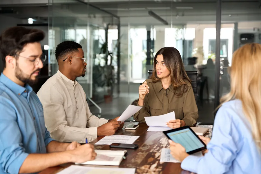 Four diverse coworkers in a modern office having a business meeting with documents and tablet on table