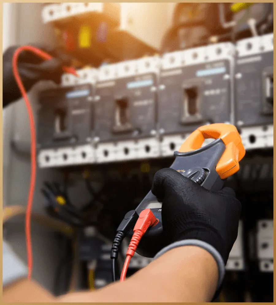 Electrician wearing gloves using a clamp meter to test current in an electrical panel with circuit breakers.