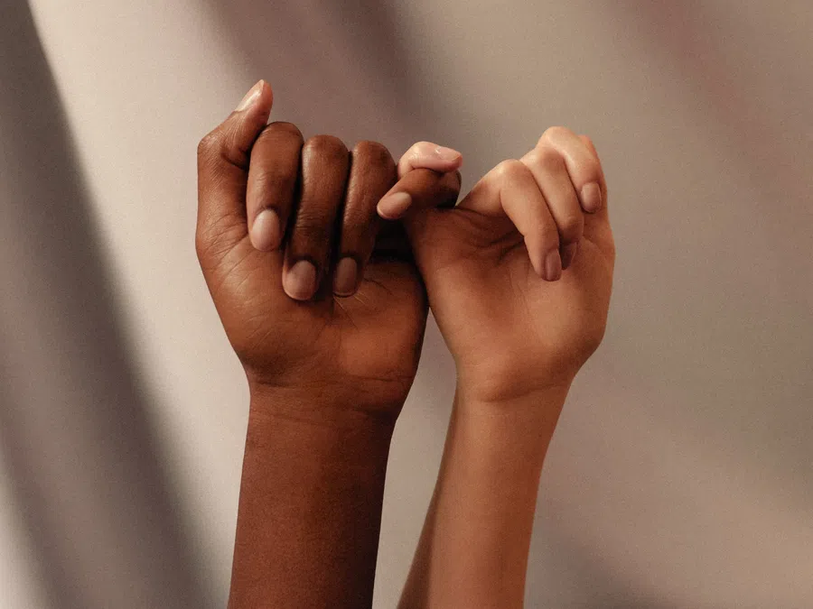 Two hands, one dark-skinned and one light-skinned, link pinky fingers symbolizing unity and promise.