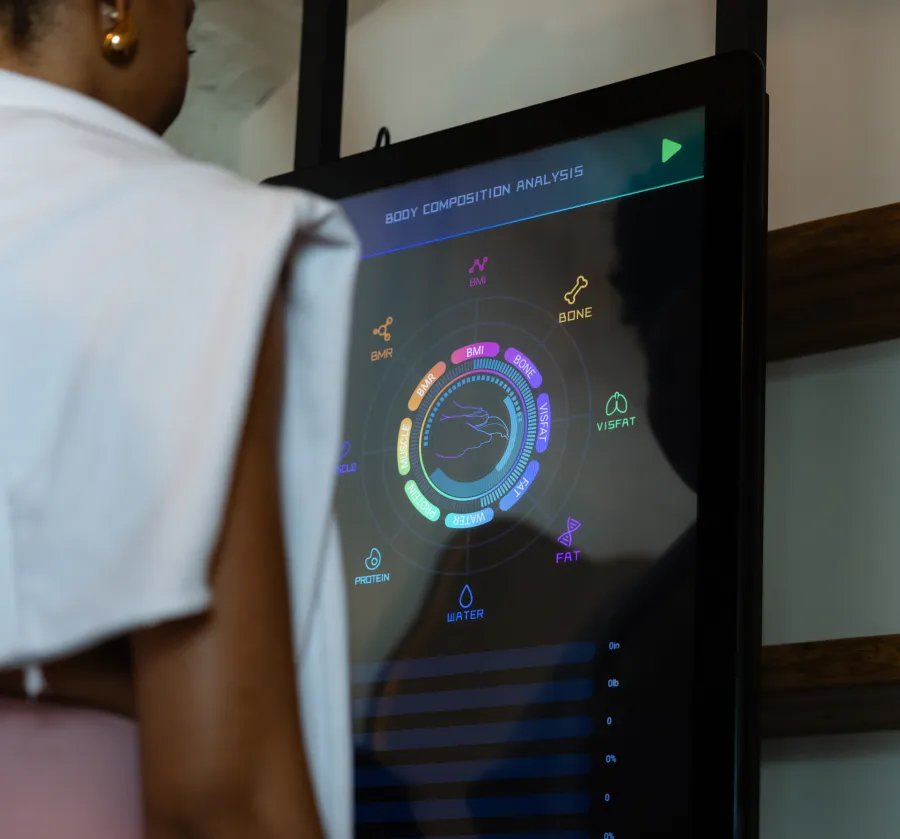 Person viewing a digital body composition analysis screen displaying BMI, bone, fat, protein, and water metrics.