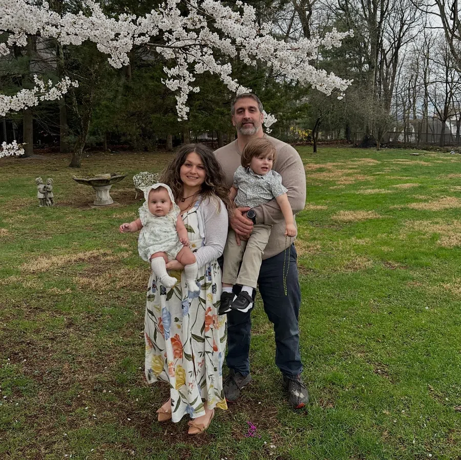 Family of four posing under blooming white cherry blossom tree in a green grassy yard during springtime