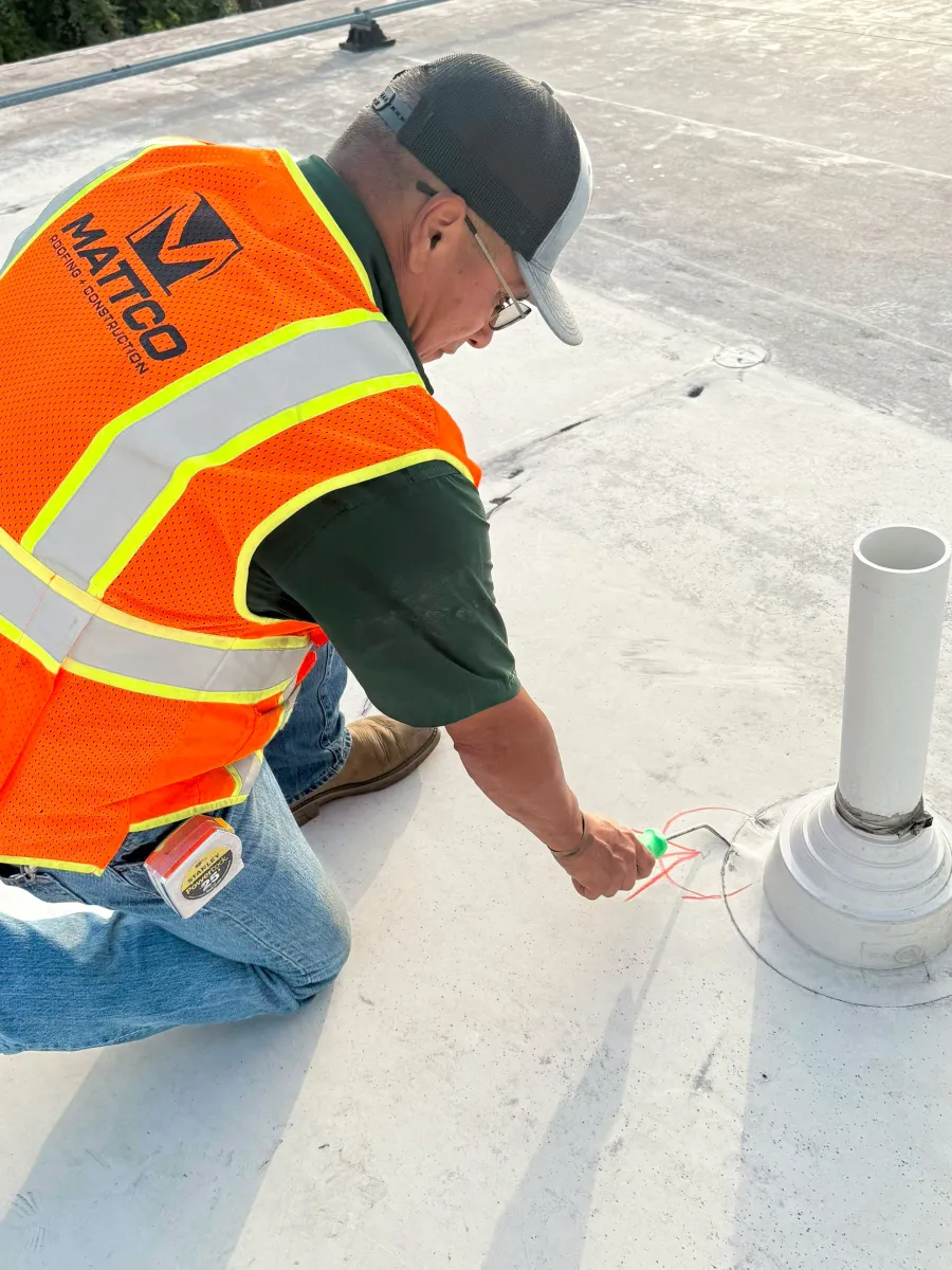 Construction worker marking a flat rooftop near a pipe wearing a bright orange safety vest and cap.