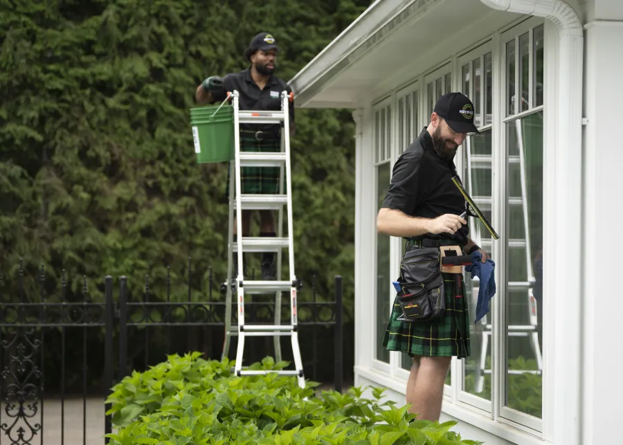 a couple of men standing outside a house with a ladder and a bucket