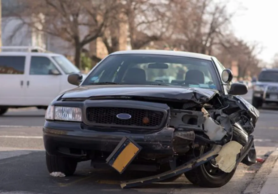 Damaged black sedan with severe front-end collision parked on city street after accident