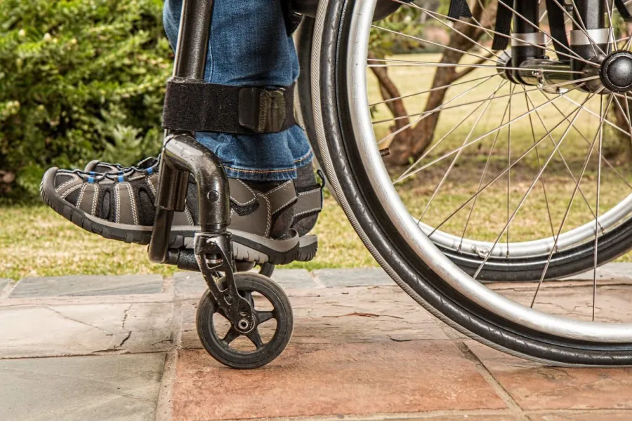 Close-up of person’s feet in a wheelchair outdoors on tiled ground with greenery in the background