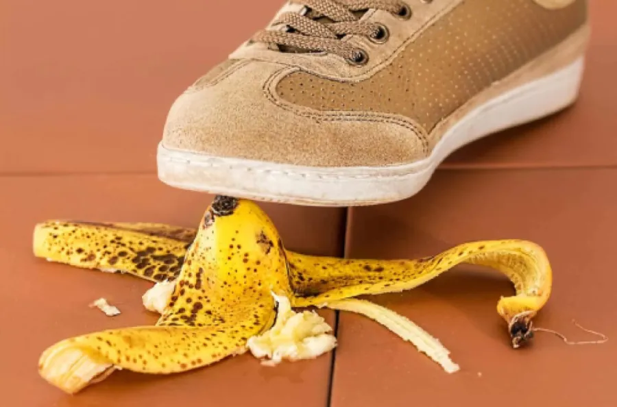 Close-up of a beige sneaker about to step on a spotted banana peel on brown floor tiles