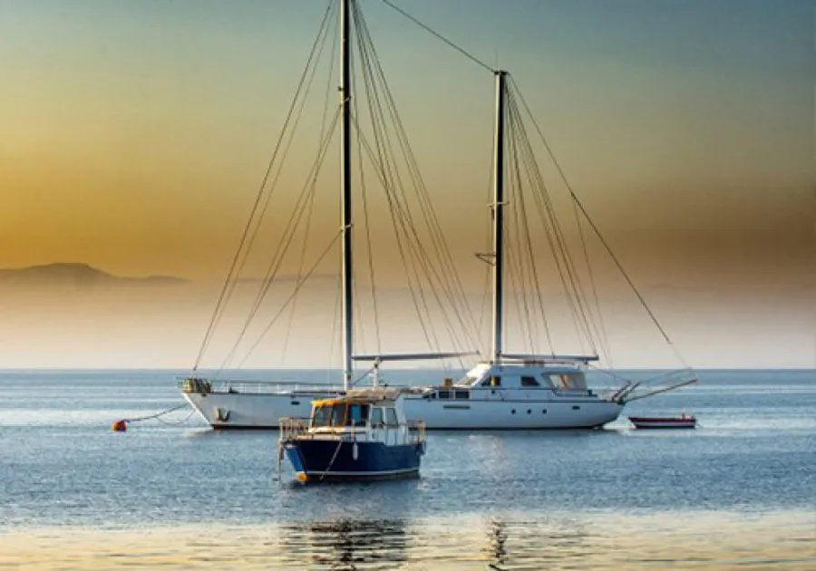 Two sailboats anchored on calm water during a golden sunset with distant mountains in the background