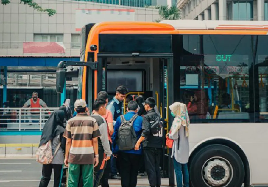 Group of diverse people boarding an orange and white city bus at a busy urban stop.
