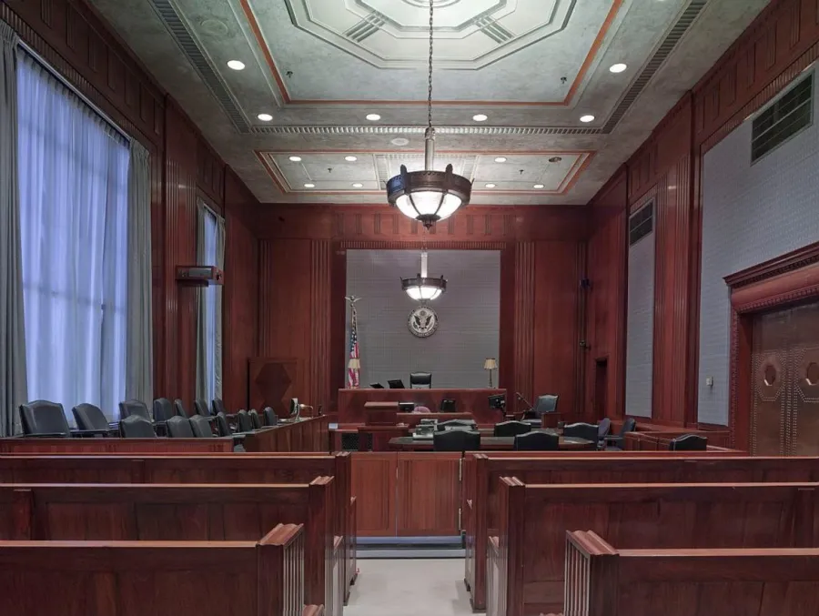 Empty courtroom with wooden benches, judge's bench, American flag, and overhead chandelier lighting