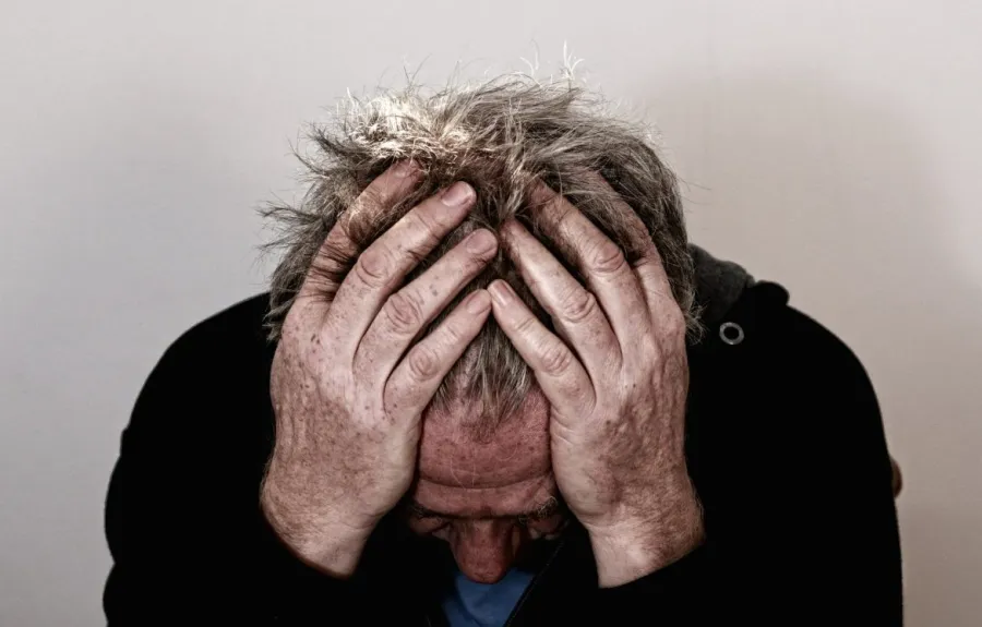 Man with gray hair holding his head in hands, showing stress or frustration against neutral background