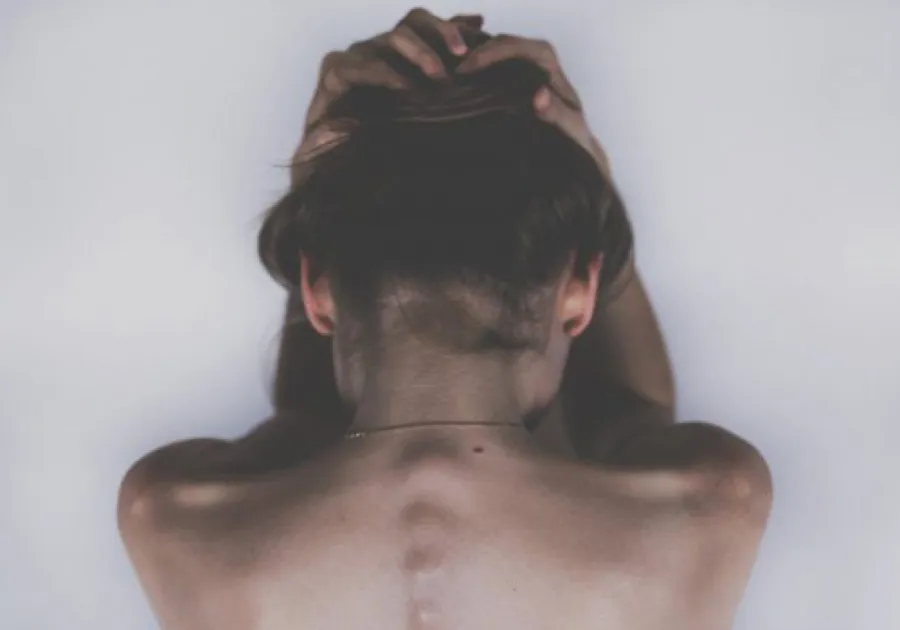 Rear view of a woman holding her head with bare back and visible spine against a neutral background