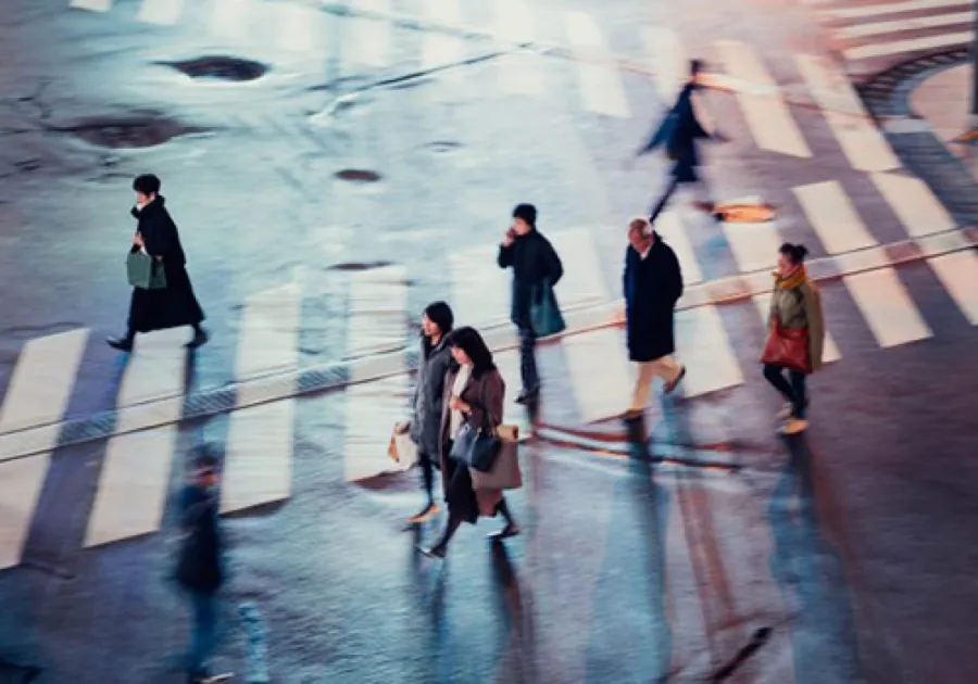 People walking across a wet crosswalk casting long shadows during daylight.