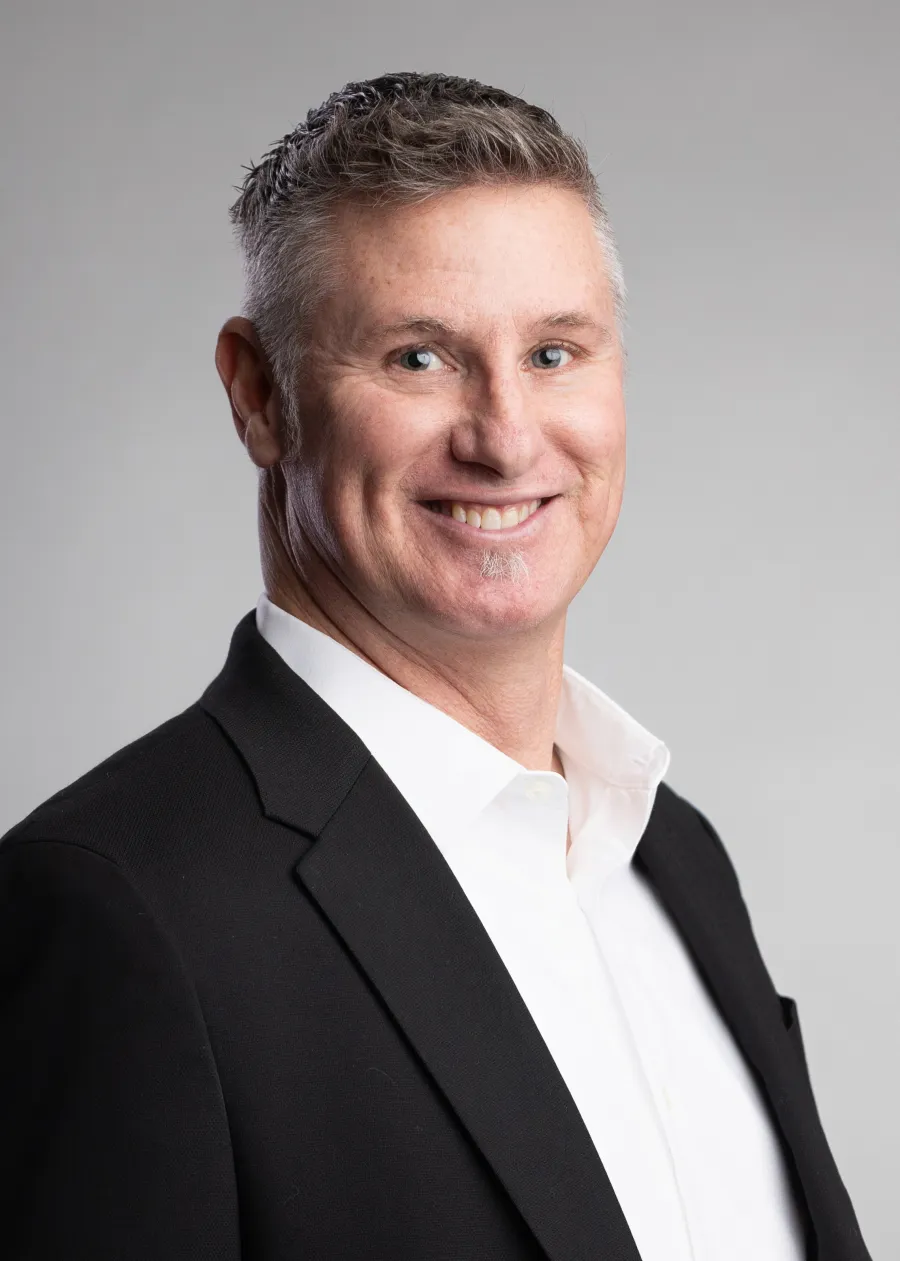 Smiling middle-aged man with gray hair wearing a black blazer and white shirt on a gray background