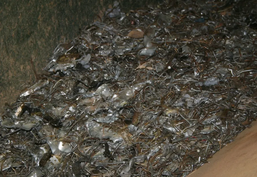 Pile of scrap metal pieces and twisted wires inside a rusty container or dumpster.