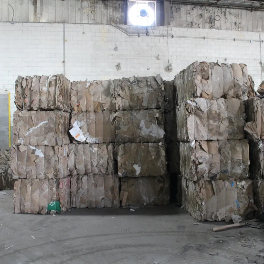 Stacked bales of compressed cardboard inside a warehouse with industrial walls and scattered debris.