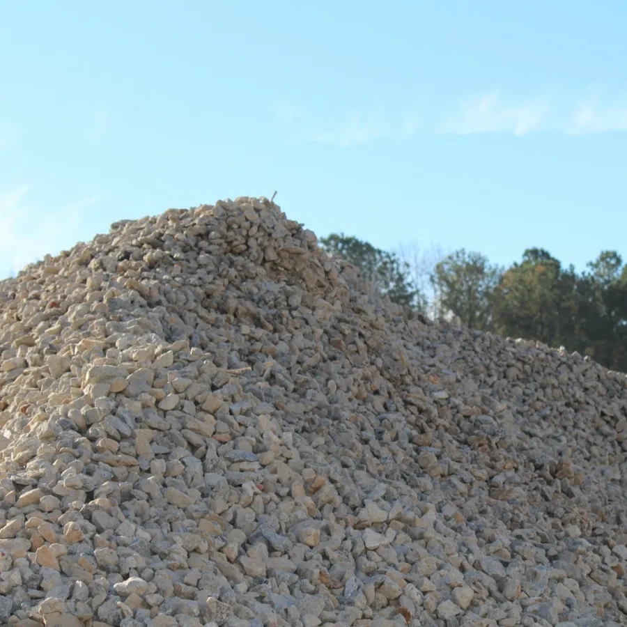 Large pile of crushed gravel stones with trees and blue sky in the background at a construction site.