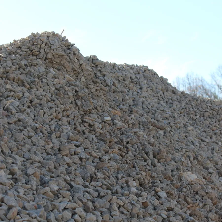 Large pile of gray crushed stones outdoors with clear sky and trees in background