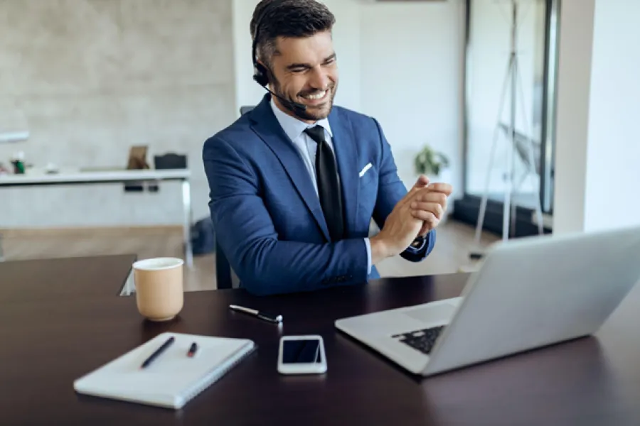 Smiling businessman in blue suit using headset and laptop during video conference at office desk