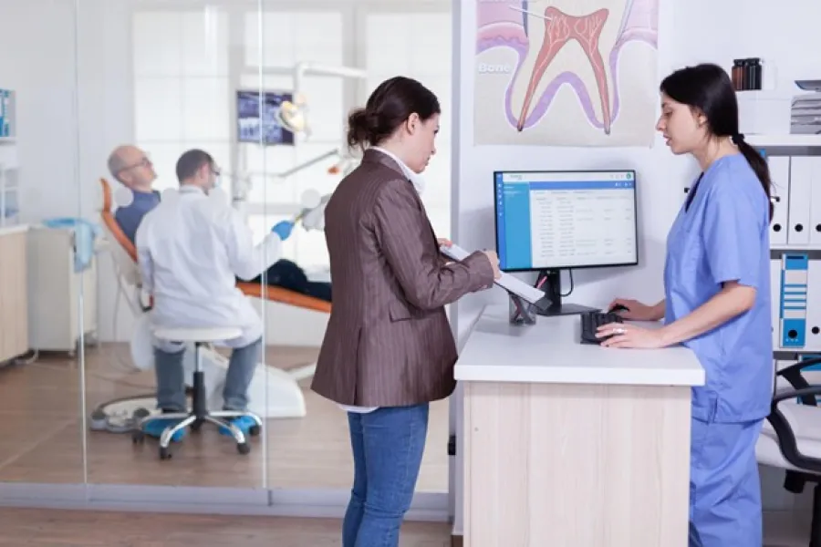 Patient consulting with dental receptionist while dentist treats another patient in background