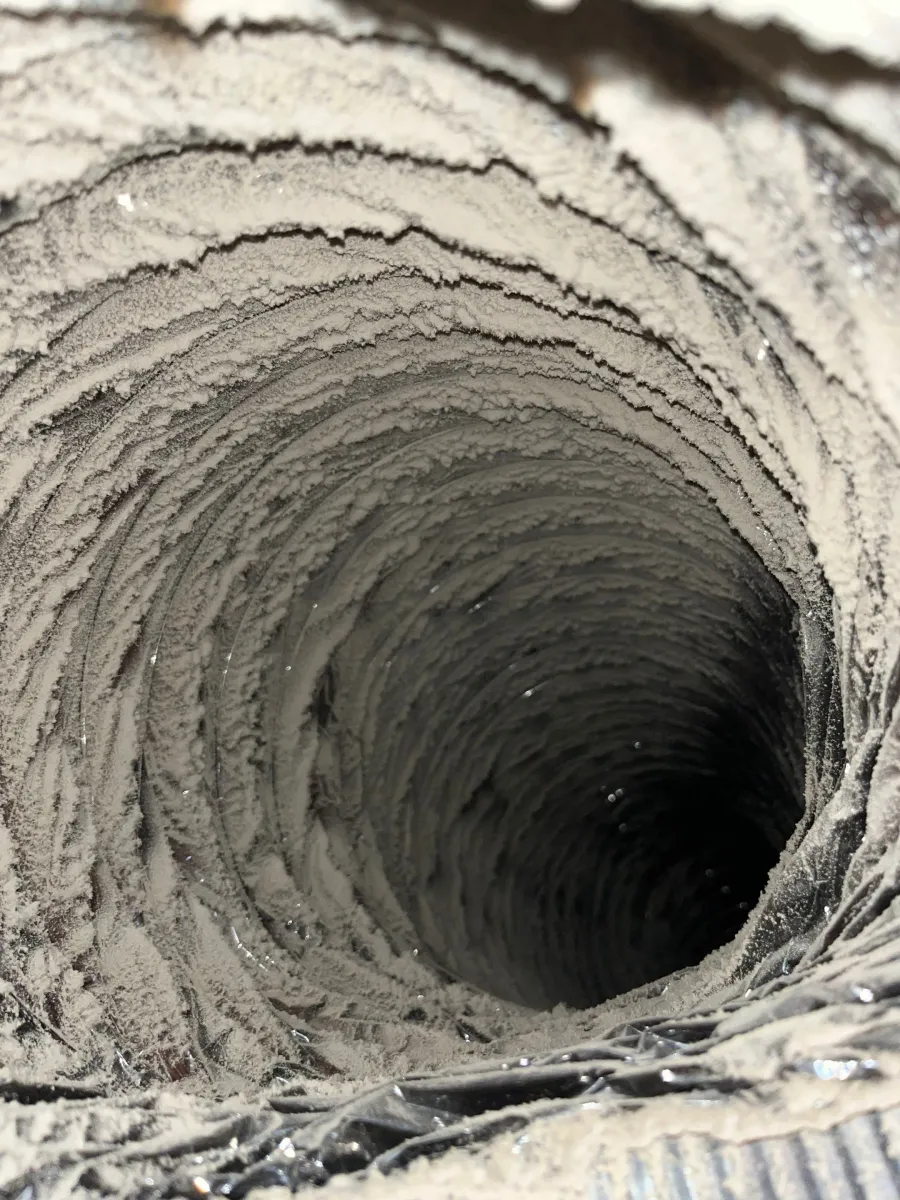 Close-up of a heavily dust-coated duct interior showing thick layers of dirt buildup in a spiral tube.