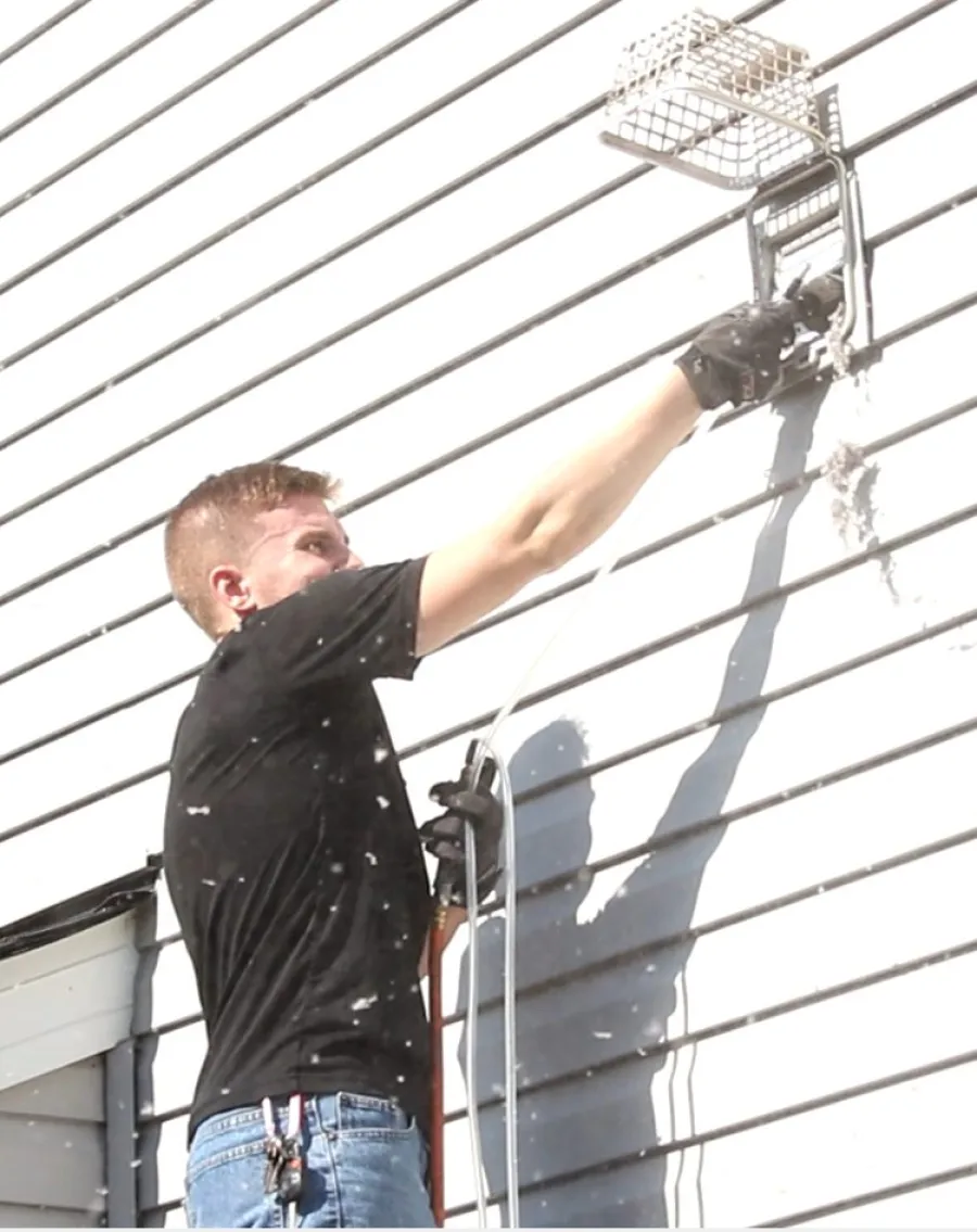 Man using a power tool to clean or remove paint from white horizontal siding on a house exterior.