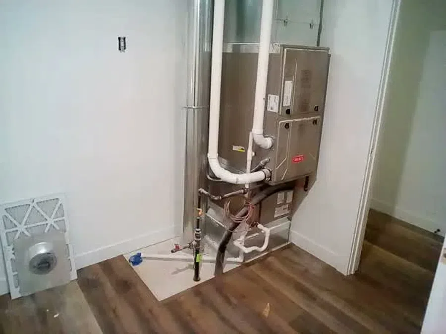 Newly installed HVAC furnace system with white PVC pipes in a room with wood flooring and white walls