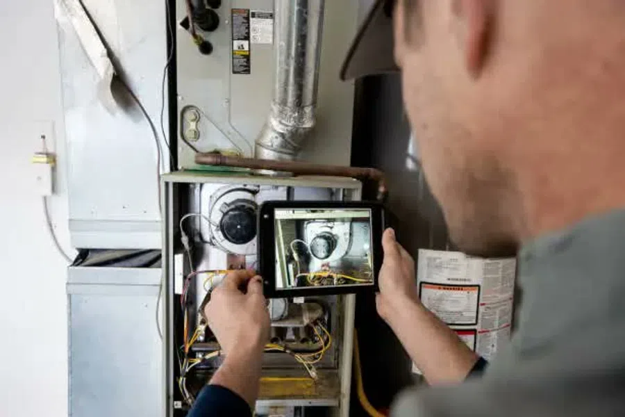 Technician inspecting furnace components using a tablet for diagnostics and maintenance work indoors.