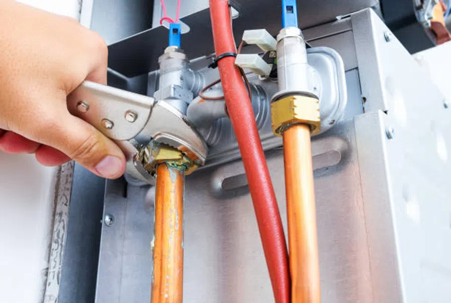Hand tightening a pipe fitting on copper plumbing with an adjustable wrench, surrounded by pipes and valves