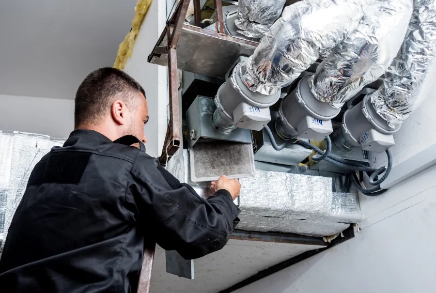 Technician inspecting HVAC ducts and machinery for maintenance in a commercial building setting.