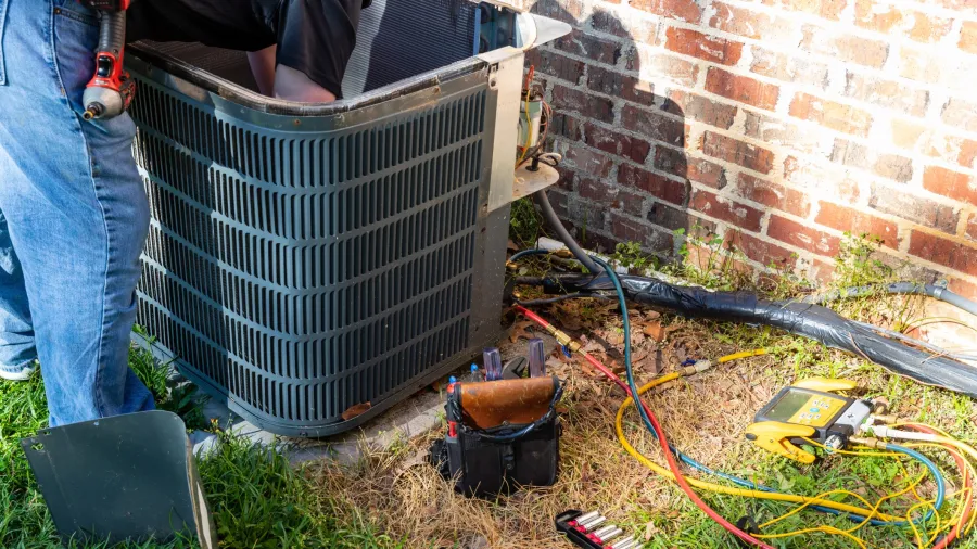 Technician repairing an outdoor air conditioning unit with tools and diagnostic equipment on the ground in Dallas, GA