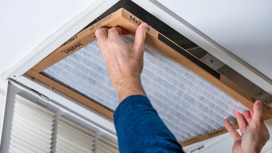 Person installing or replacing a rectangular air filter in a ceiling vent with white louvers in Dallas, GA