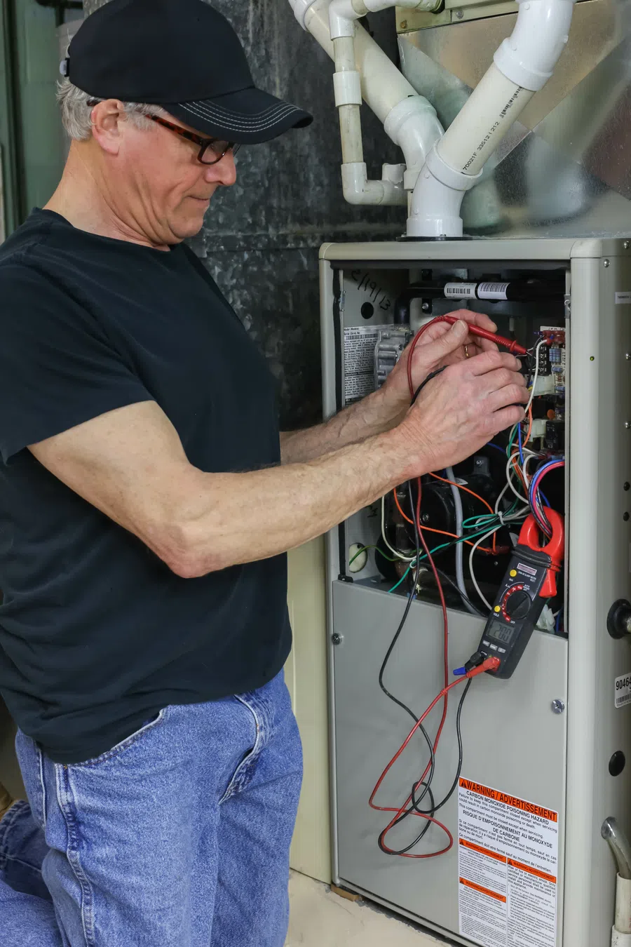 Technician troubleshooting electrical components in a furnace with multimeter and tools.