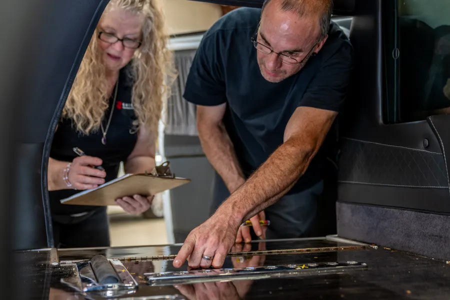 Two professionals inspecting and measuring the interior floor of a vehicle for customization or repair work.