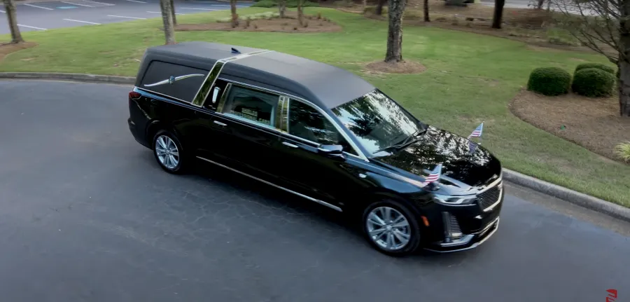 Black luxury hearse parked on a curved driveway surrounded by green grass and trees.