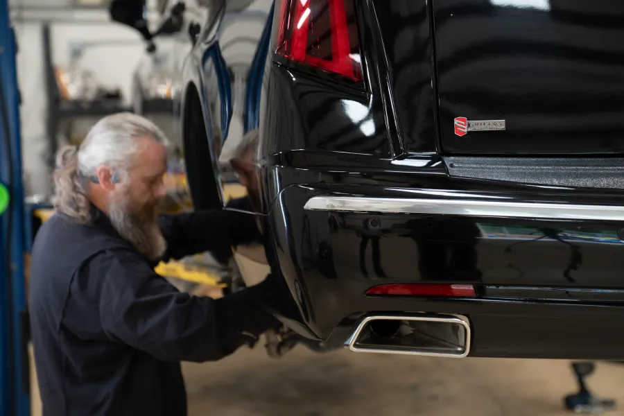 Mechanic with grey beard working on the rear wheel of a black car in a garage workshop.