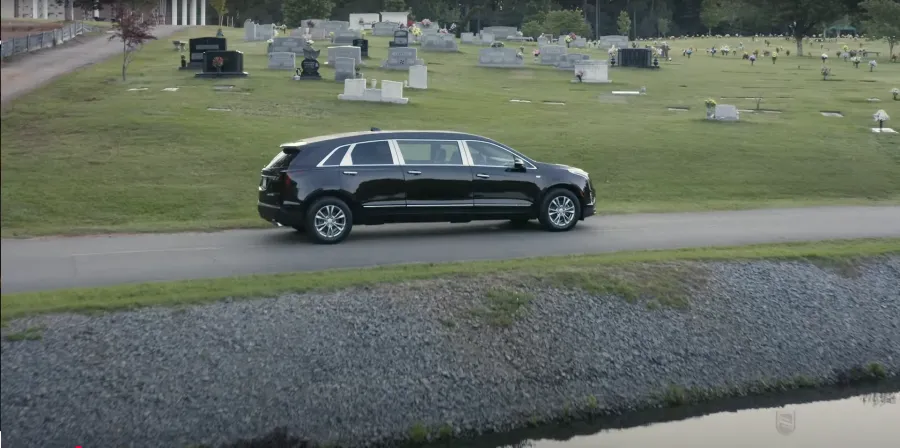 A sleek black SUV driving along a path next to a cemetery, surrounded by gravestones.
