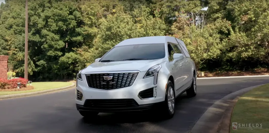 A sleek silver Cadillac SUV parked on a curved road surrounded by greenery.