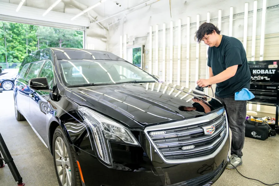 Technician polishing the hood of a black Cadillac limousine in a well-lit garage.