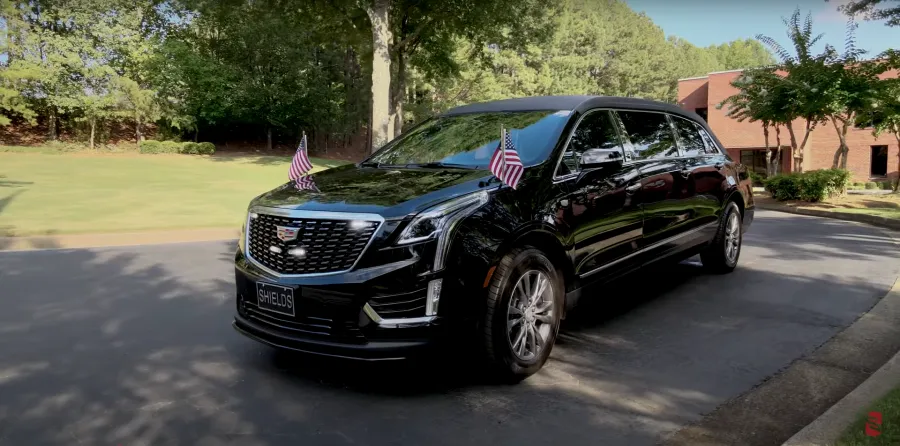A sleek black Cadillac SUV adorned with American flags parked on a well-maintained driveway.