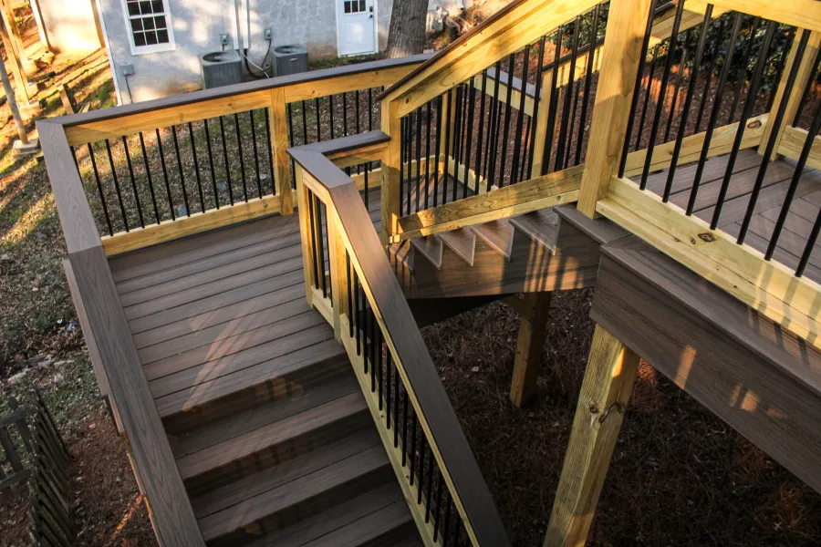 Outdoor wooden deck with stairs and black metal railings in natural backyard setting during daytime