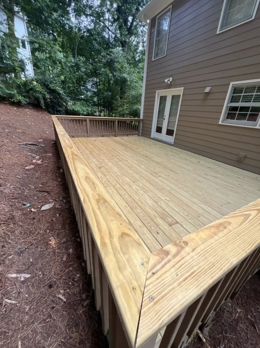 Newly built wooden deck attached to a house surrounded by trees and natural mulch ground cover.