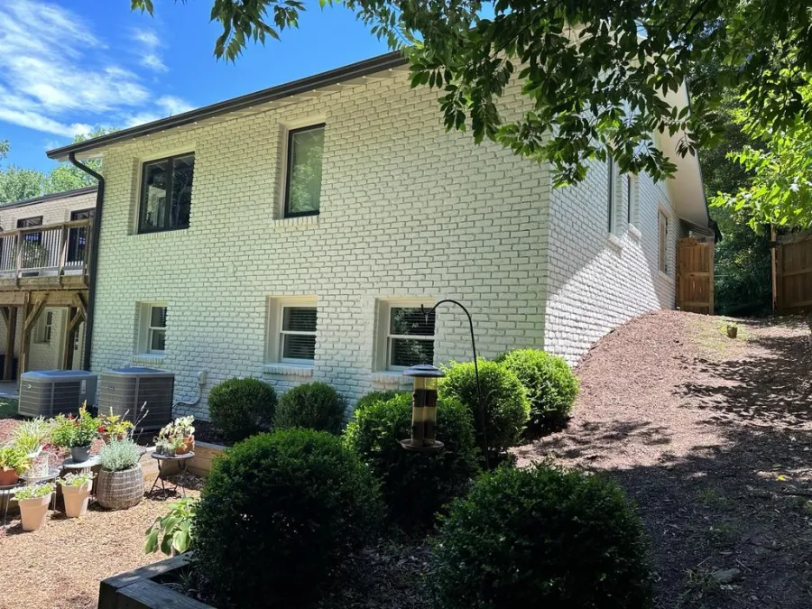 Green house exterior with white garage door, black window shutters, surrounded by trees and blue sky.