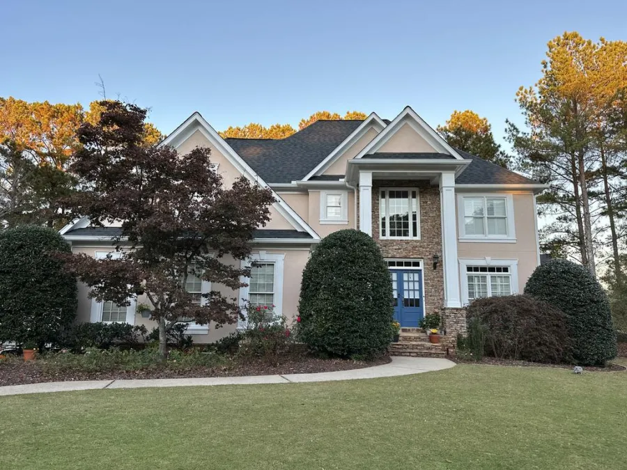 Close-up of a beige house exterior with dormer windows and gray shingles on a sunny day.