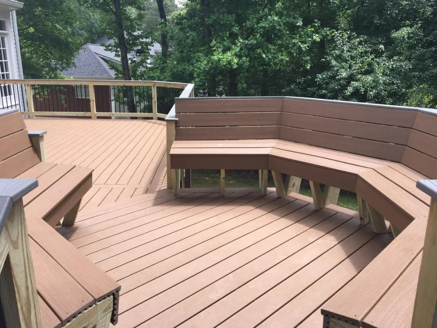 Newly built wooden deck attached to a house with brown siding and surrounding trees in the background
