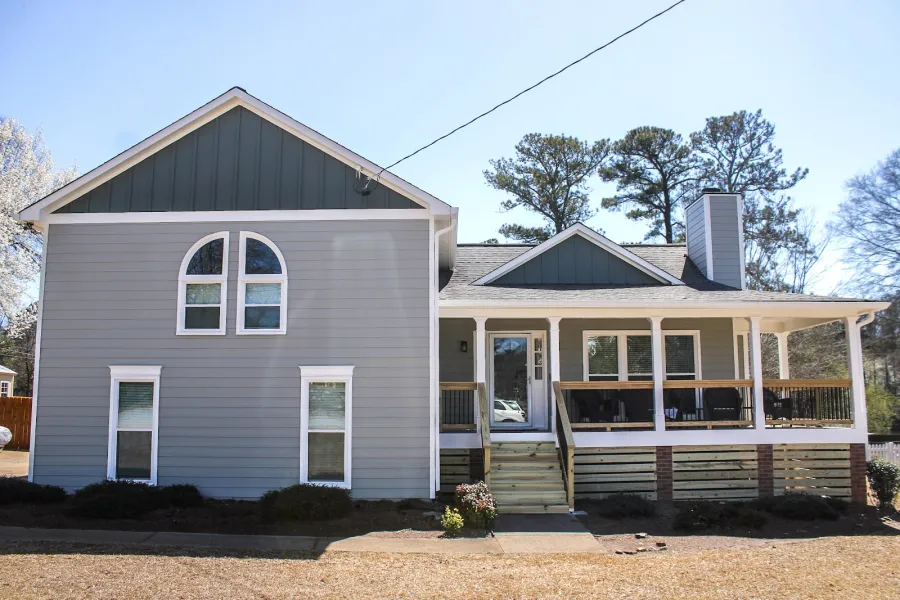 Gray two-story house with white trim, front porch, and multiple windows under a clear blue sky.